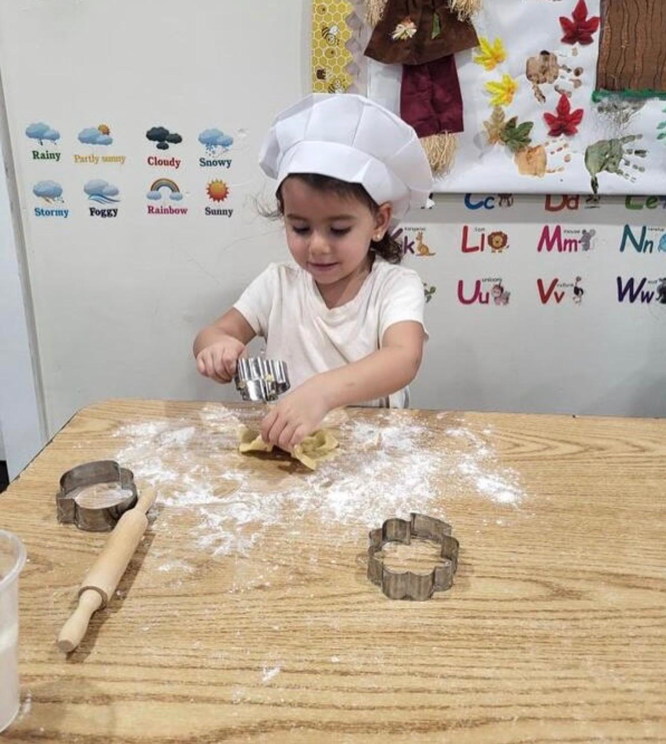 A child rolling dough in a chef hat